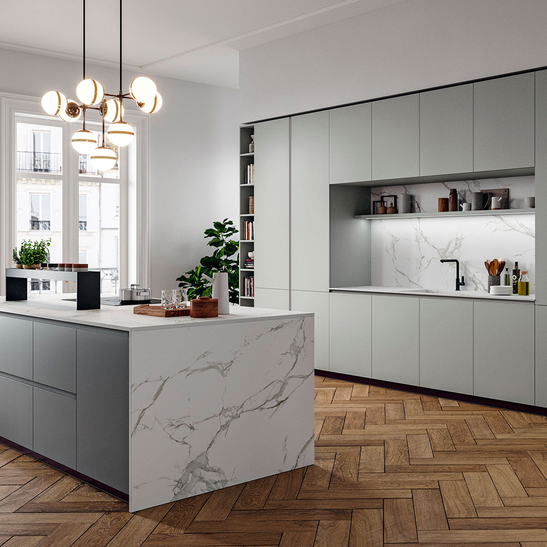 Interno di una cucina moderna con armadietti grigi, piano cucina in marmo bianco e parquet in legno. Illuminazione elegante e piante decorative.