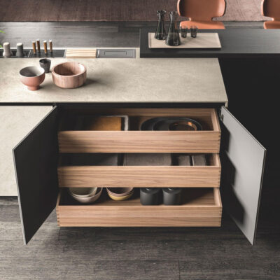 Cassetti di un mobile da cucina con ripiani in legno chiaro, contenenti utensili, piatti e accessori da cucina ordinati.