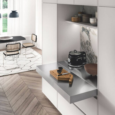 Vista di una cucina moderna con piano di lavoro in acciaio inox, elettrodomestici e stoviglie eleganti, illuminata da luce naturale.