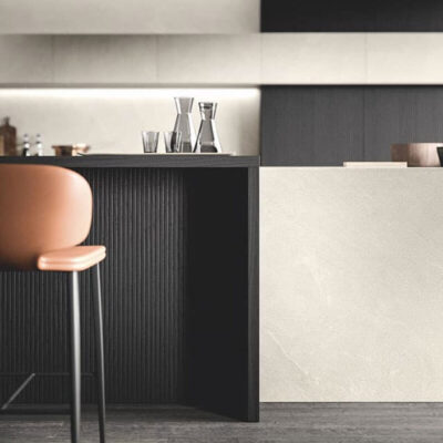 Vista ravvicinata di un elegante bancone da cucina con finiture nere e bianche, un seggio in pelle arancione e bicchieri trasparenti.