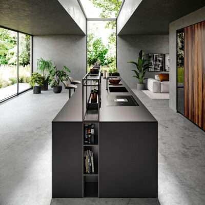 Interiore moderno di una cucina minimalista, con isola centrale in nero, piante decorative e ampie finestre che offrono una vista verde e luminosa.