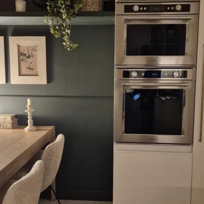 Una cucina moderna con pareti scure, un grande tavolo in legno e un forno a doppio scomparto. Dettagli eleganti e minimalisti.