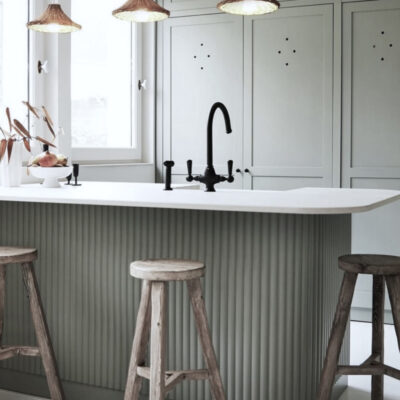 Una moderna cucina con un'isola bianca, un lavello nero e sgabelli in legno. Le pareti sono di un verde chiaro, creando un'atmosfera elegante e accogliente.