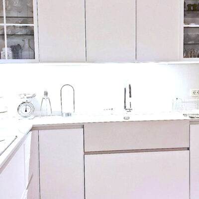 Cucina moderna e minimalista con armadietti bianchi, piano cottura e lavello illuminati. Contenitori e stoviglie ben organizzati.