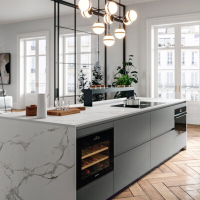 Vista di una moderna cucina minimalista con isola centrale in marmo, piantane verdi e luce naturale che entra dalle finestre.