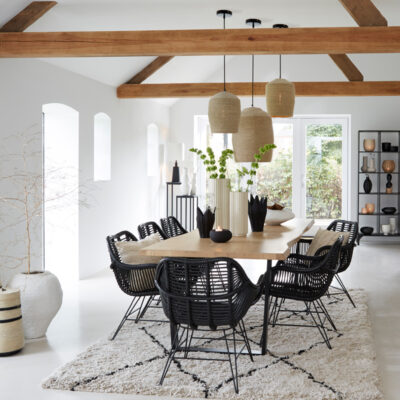 Interno di una sala da pranzo moderna con tavolo in legno, sedie nere intrecciate e lampade pendenti in juta. Dettagli decorativi eleganti e accoglienti. Illuminazione elegante
