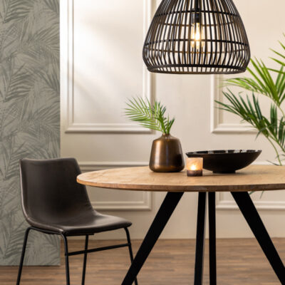 Un tavolo rotondo in legno con una moderna lampada a sospensione sopra, decorato con piante ornamentali e candele. Una sedia nera in stile contemporaneo completa l'ambiente elegante. Illuminazione