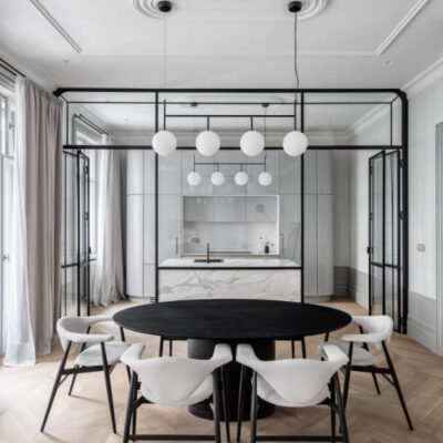 Illuminazione moderna. Interno di una cucina moderna e minimalista con arredo elegante, illuminata da lampade sferiche. Tavolo ovale nero e sedie bianche si abbinano a armadi grigi e dettagli in marmo.