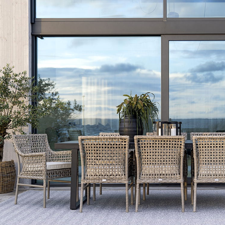 Spazio esterno arredato con un tavolo e sedie in rattan, pianta decorativa e vista su un cielo nuvoloso.