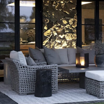 Un'area salotto all'aperto con mobili in rattan grigio, cuscini eleganti e un tavolino. Una lampada crea un'atmosfera accogliente.