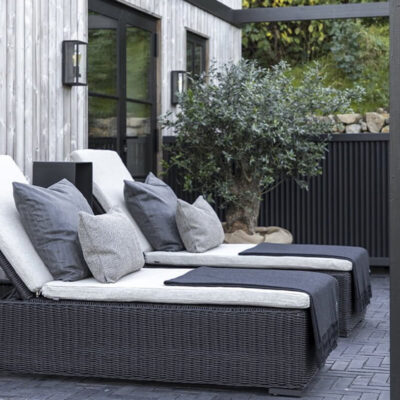Due lettini reclinabili con cuscini, situati in un'area esterna elegante e tranquilla, circondati da vegetazione.