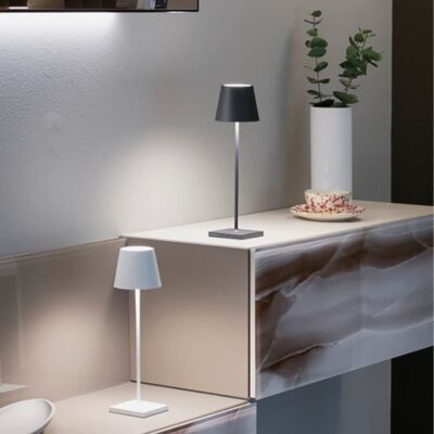 Composizione di illuminazione moderna con lampade da tavolo in stile minimalista su un mobile elegante, accompagnate da pianta e piatto decorativo.