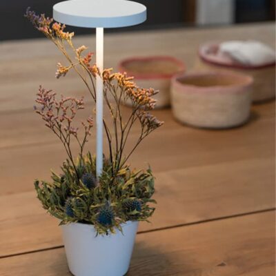 Un centro tavola elegante con una candela bianca e un bouquet di fiori secchi, su un tavolo in legno. Sullo sfondo si intravedono cesti decorativi.
