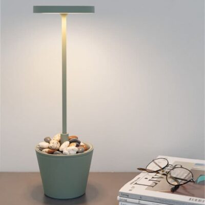 Lampada moderna con basa a forma di vaso pieno di sassi colorati e luce soffusa, su un tavolo con occhiali.