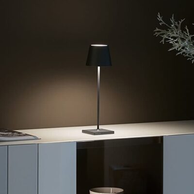 Una lampada da tavolo elegante con paralume nero su un tavolino bianco, illuminato da una luce soffusa, creando un'atmosfera moderna.